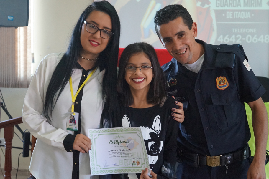 A Professora Micaela junto ao GCM Ramiro Garcia entregam o certificado à Alexandra Melo.